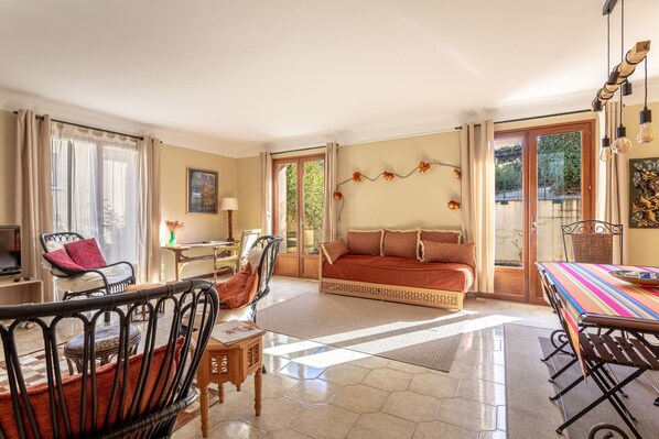 A spacious living area with a sofa, chairs, a dining table, and a view through the glass door.