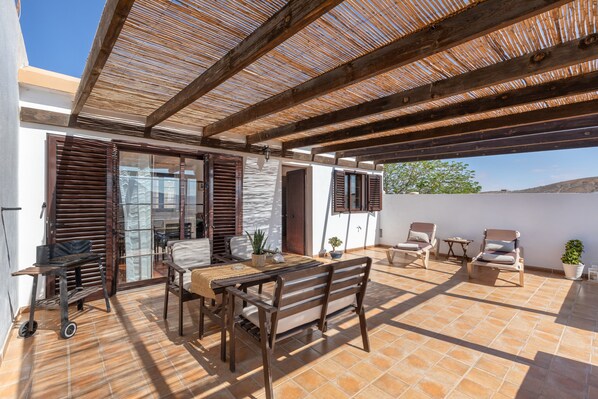 Un patio al aire libre con una mesa de madera, sillas y una parrilla.