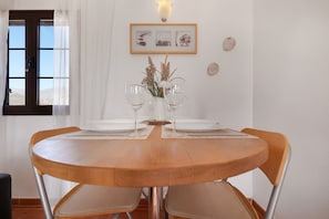 A round wooden dining table with four chairs, a vase with dried flowers, and a framed picture on the wall.