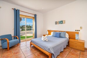 Une chambre à coucher comprenant un lit, une chaise, une table de chevet et une vue sur l’extérieur, accessible par une porte coulissante.