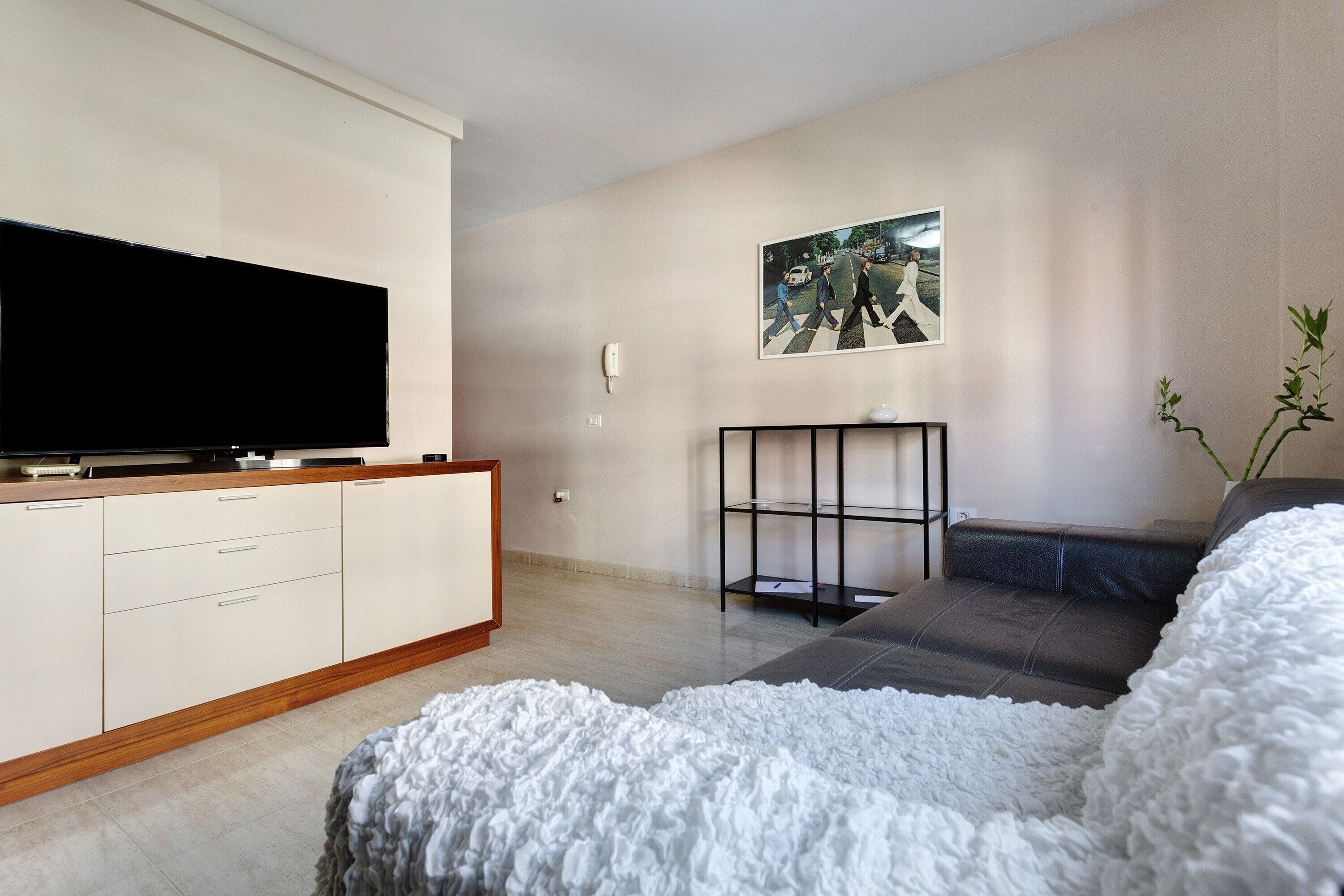 Ein modernes Schlafzimmer mit einem großen Flachbildfernseher, einer Couch, einem weißen, flauschigen Teppich und einem gerahmten Bild an der Wand.