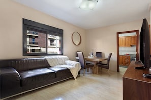 A living room with a leather sofa, a dining table with chairs, a TV, and a kitchen area visible through an open door. - Vacation Apartment 'Apartamento Romo' with Sea View and Wi-Fi (Candelaria)