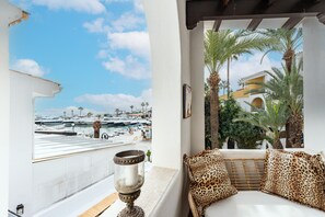 Un balcon donnant sur un port de plaisance, un canapé blanc agrémenté de coussins à motifs léopard et un vase décoratif en verre.