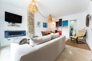 A living room with a flat-screen TV, a sofa, a dining area with a table and chairs, and a modern chair. - Apartment 'Mi Patio, Port Of Cabopino' with Shared Pool, Wi-Fi and Air Conditioning (Unknown)