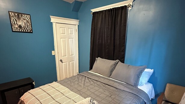 Un dormitorio con cama, mesita de noche, silla, puerta y una obra de arte con cebras en la pared.
