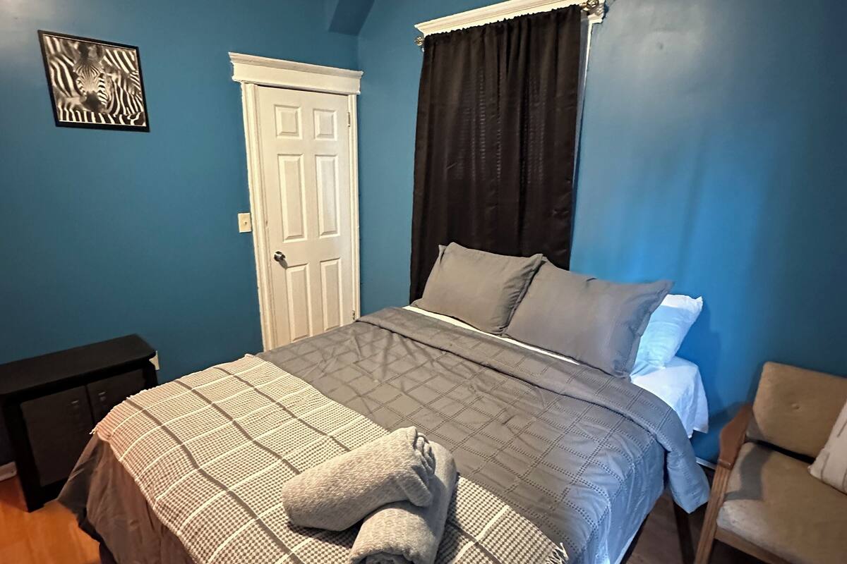 A bedroom with a bed, a nightstand, a chair, a door, and a zebra artwork on the wall.