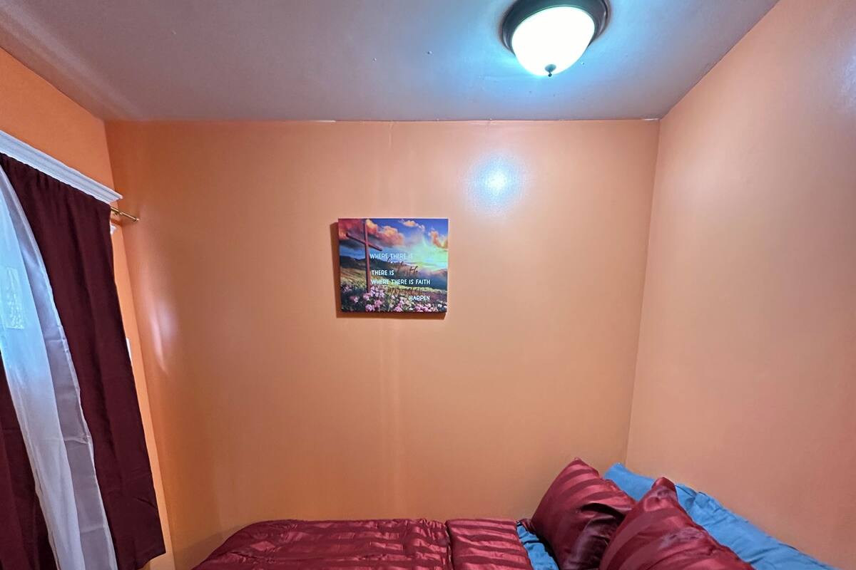 A room with a bed, a window with curtains, and a ceiling light.