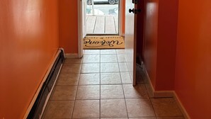 Un pasillo con paredes anaranjadas, una puerta que da al exterior y un felpudo con la inscripción 'Welcome Home'.
