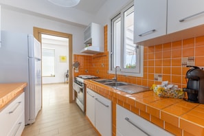 A modern kitchen with white cabinets, an orange tiled backsplash, a stainless steel sink, and a coffee maker.