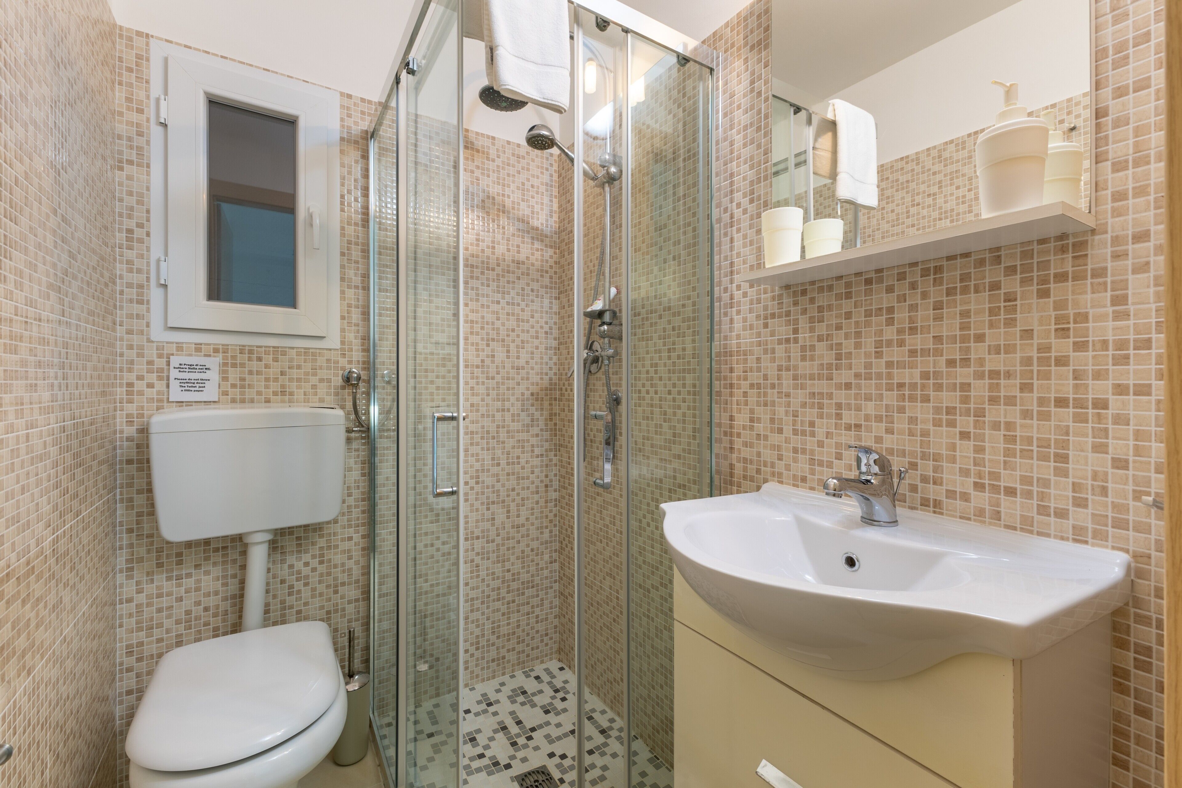 A bathroom with a glass-enclosed shower, a toilet, a sink, and a mirror.