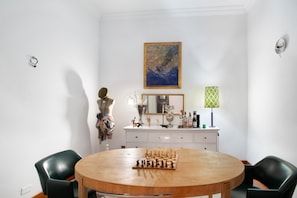 A dining area with a round wooden table, chess set, two black chairs, a white dresser with decorative items, and a painting on the wall. - Vacation Apartment 'Suitme Teror' with Wi-Fi (Teror)