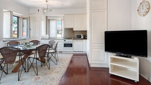 A modern kitchen with white cabinets, a dining table with chairs, a TV on a stand, and a large window. - Apartment 'Appartamento Gabbiano' with Shared Terrace, Wi-Fi and Air Conditioning (Rapallo)