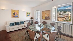 A dining area with a glass table, wicker chairs, a white sofa, and artwork on the walls. - Apartment 'Appartamento Gabbiano' with Shared Terrace, Wi-Fi and Air Conditioning (Rapallo)