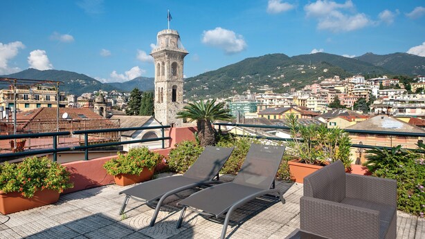 A rooftop terrace with lounge chairs, potted plants, and a view of a historic tower and cityscape. - Apartment 'Appartamento Gabbiano' with Shared Terrace, Wi-Fi and Air Conditioning (Rapallo)