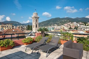 A rooftop terrace with lounge chairs, potted plants, and a view of a historic tower and cityscape. - Apartment 'Appartamento Gabbiano' with Shared Terrace, Wi-Fi and Air Conditioning (Rapallo)
