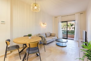 Un salon moderne avec une table ronde en bois, quatre chaises, un canapé, une petite table ronde et une grande fenêtre avec des rideaux.
