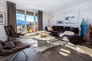 A modern living room with a sofa, chairs, a coffee table, and a view of mountains through large windows.