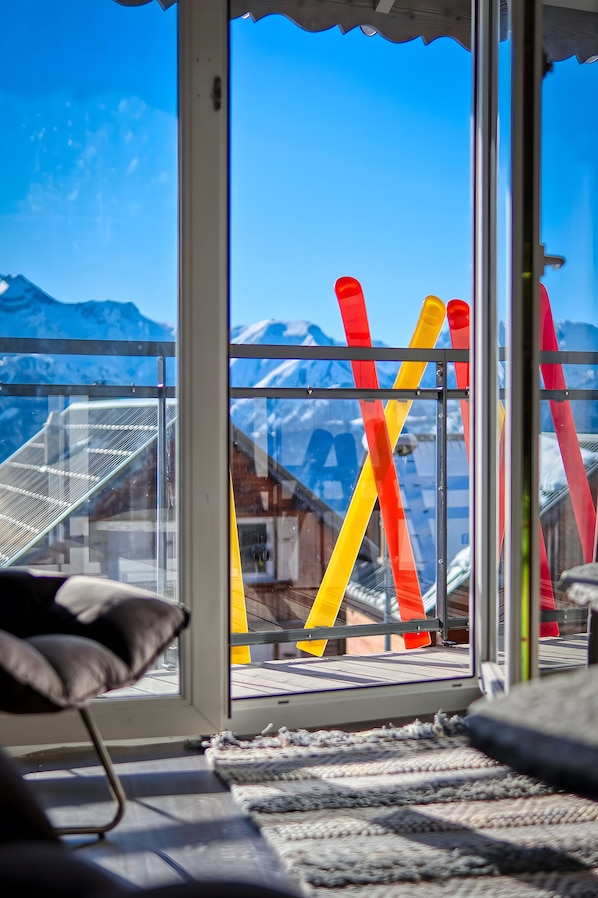 A room with a view of snow-covered mountains through large windows, a chair, and a patterned rug.