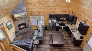 Een gezellig cabin interieur met een stenen open haard, een zithoek met een bank en salontafel, een keuken met moderne apparatuur en een eettafel.