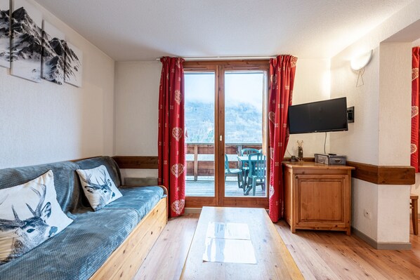 Habitación con sofá, televisión, mueble de madera y vistas a una terraza y montañas.