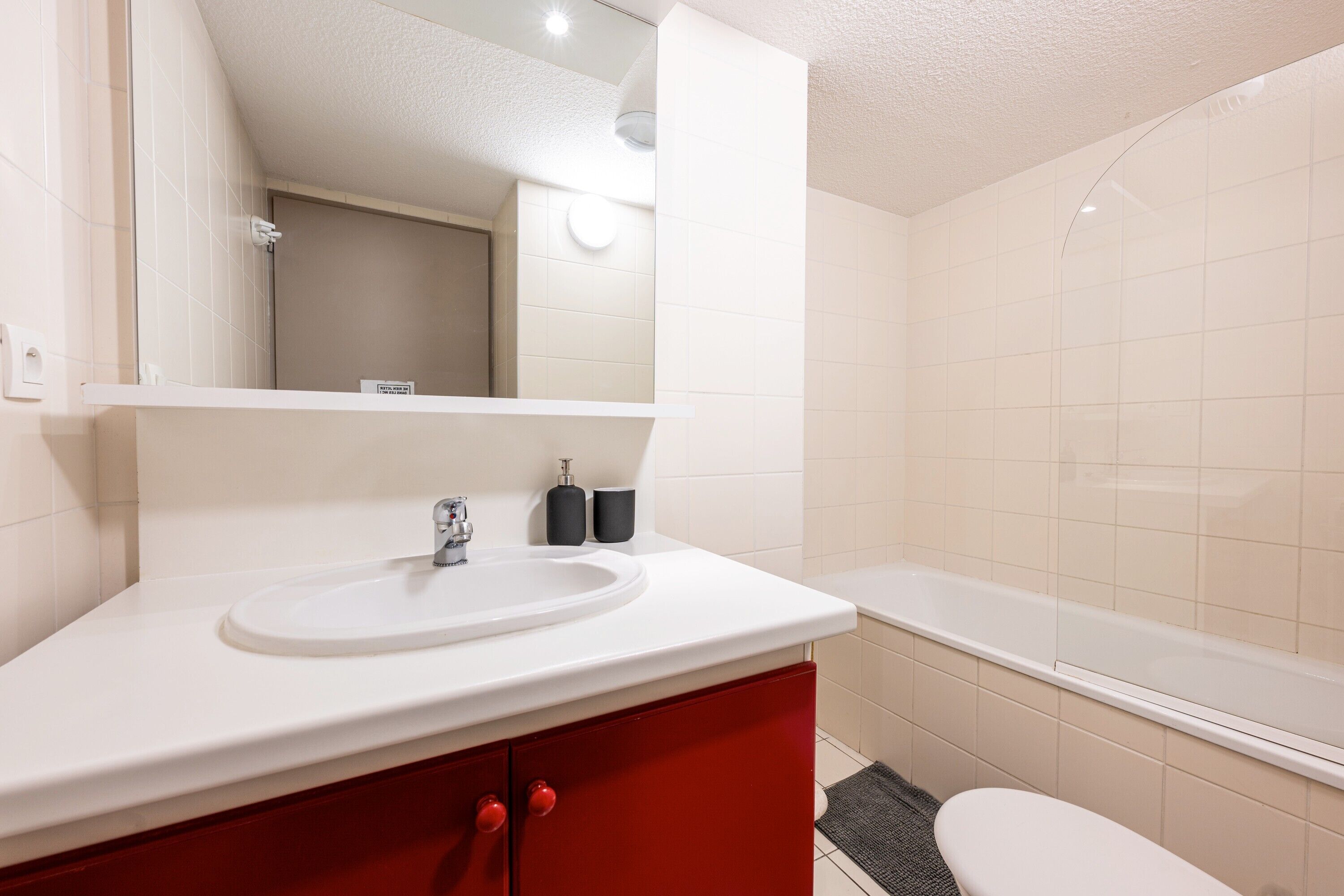 A bathroom with a white sink, red cabinet, and a bathtub.