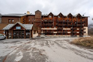 A multi-story wooden building with balconies, a parking area, and a sign indicating a restaurant.
