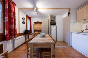 Una cocina compacta con una mesa de madera, armarios blancos y una cortina roja.