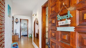 Una puerta de madera con un cartel que dice 'Beach is my Happy Place', un pasillo con un espejo y un pequeño estante azul con objetos decorativos.