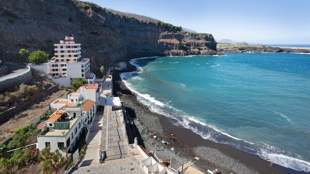 Un hotel frente al mar, con vista a un acantilado rocoso y una playa.