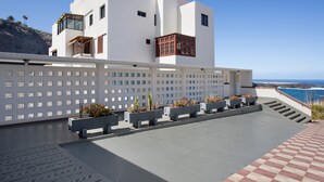 Un edificio moderno con fachada blanca, un balcón con plantas en macetas y vistas al océano.