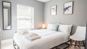 A modern bedroom with a large bed, a bedside table with a lamp, and two framed pictures on the wall. - The Red House, Leiston - A Smart Base for Coast and Work (Suffolk)