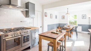 A modern kitchen with a gas stove, oven, and a wooden table with chairs. - The Red House, Leiston - A Smart Base for Coast and Work (Suffolk)