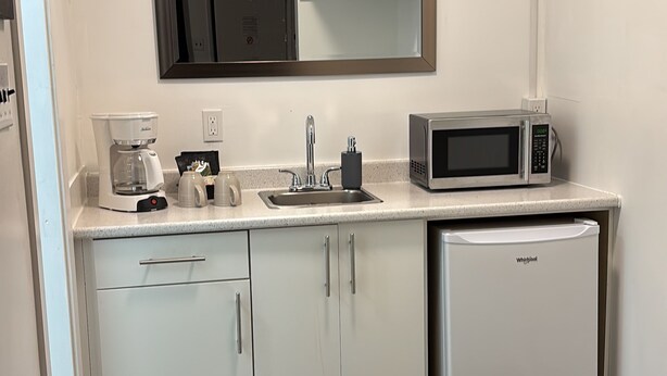 A compact kitchen with white cabinets, a coffee maker, a microwave, and a small refrigerator. - Ashcroft Motel (Ashcroft)