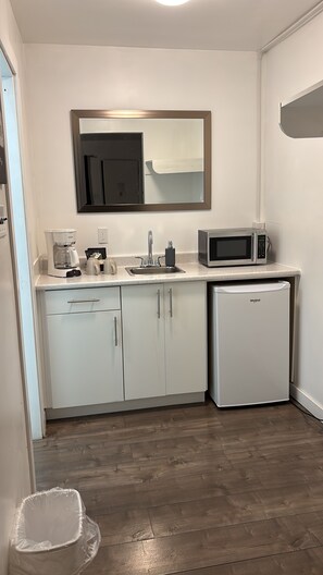 Une cuisine compacte avec des meubles blancs, une machine à café, un four à micro-ondes et un petit réfrigérateur.