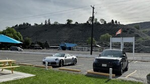 A parking area with two cars, a picnic table, and a flag. - Ashcroft Motel (Ashcroft)