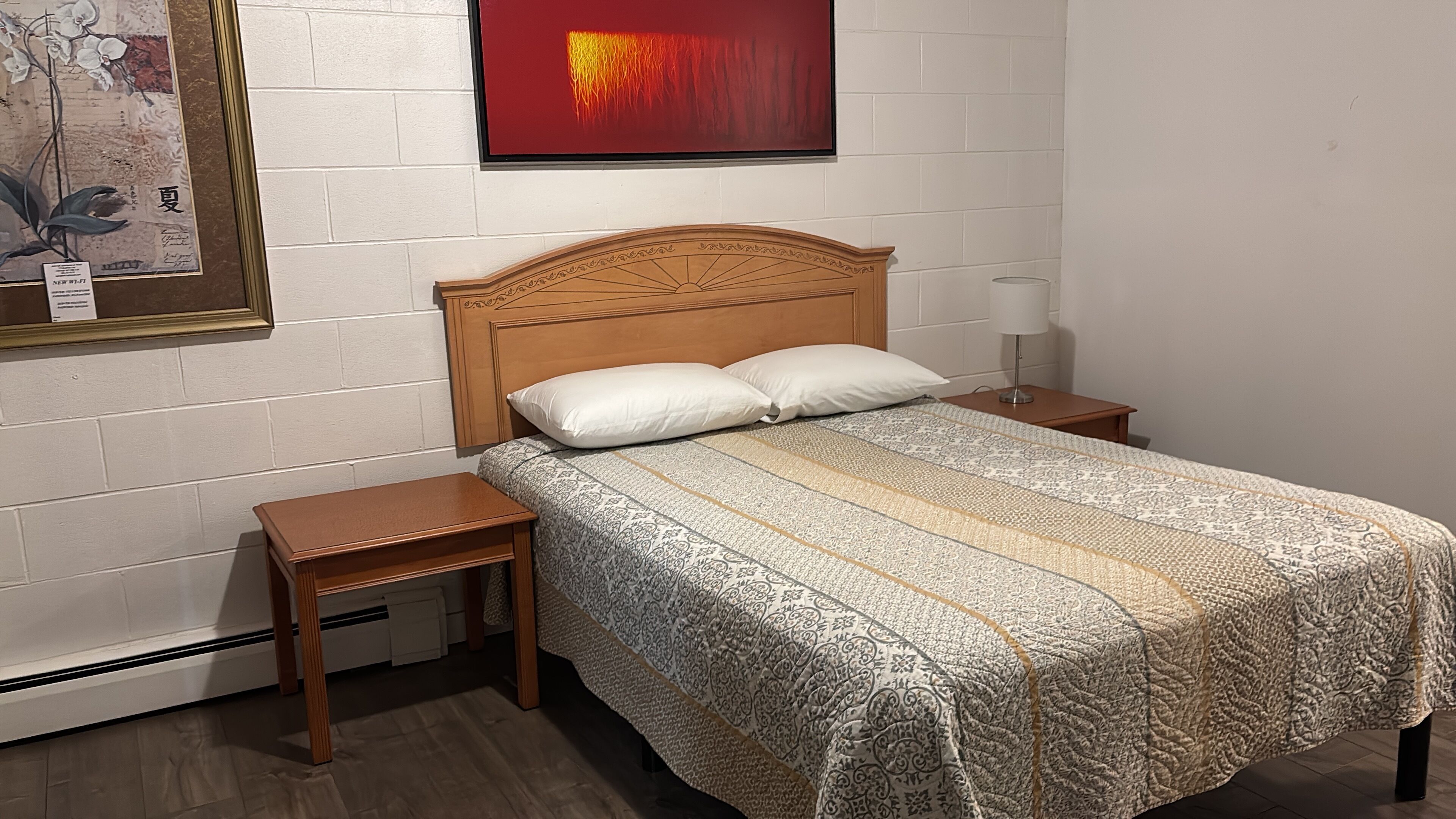 Un dormitorio con cabecera de madera, colcha estampada, dos mesitas de noche y una mesita con lámpara.