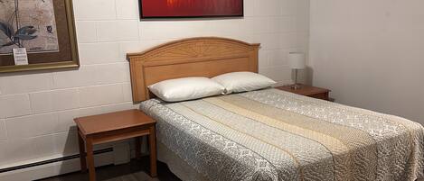 Un dormitorio con cabecera de madera, colcha estampada, dos mesitas de noche y una mesita con lámpara.