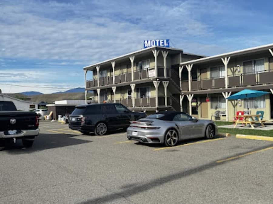 Un motel composé d’un bâtiment à deux étages, d’un parking où sont garées plusieurs voitures et, au-dessus, un ciel dégagé.