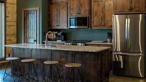 A kitchen with wooden cabinets, a stainless steel refrigerator, and a bar area with stools. - Cozy 4 bedroom Lodge close to I-30 and local wedding venues (Simms)