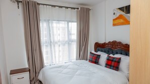 A bedroom with a large bed, a nightstand, and a window with curtains.