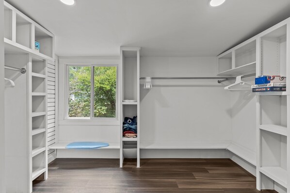 Un dressing accessible sans porte, avec des étagères blanches, un banc et une fenêtre donnant sur un espace verdoyant.