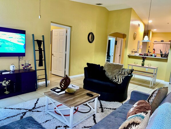 A living room with a TV, a coffee table, a sofa, and a dining area with a table and chairs.