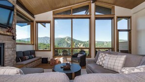 A spacious living room with a stone fireplace, large windows offering mountain views, and comfortable seating.