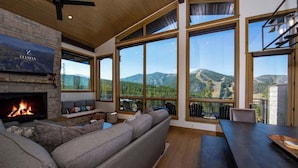 A modern living room with a fireplace, large windows, and a view of mountains.