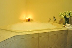 A bathroom with a large bathtub, a small candle, and a vase with flowers.