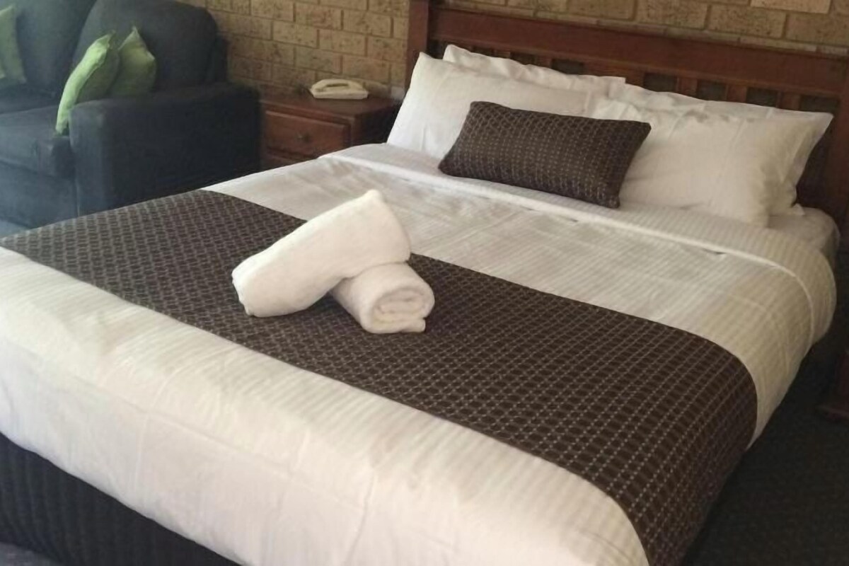 A neatly made bed with a brown and white bedspread, a folded towel, and a wooden headboard.