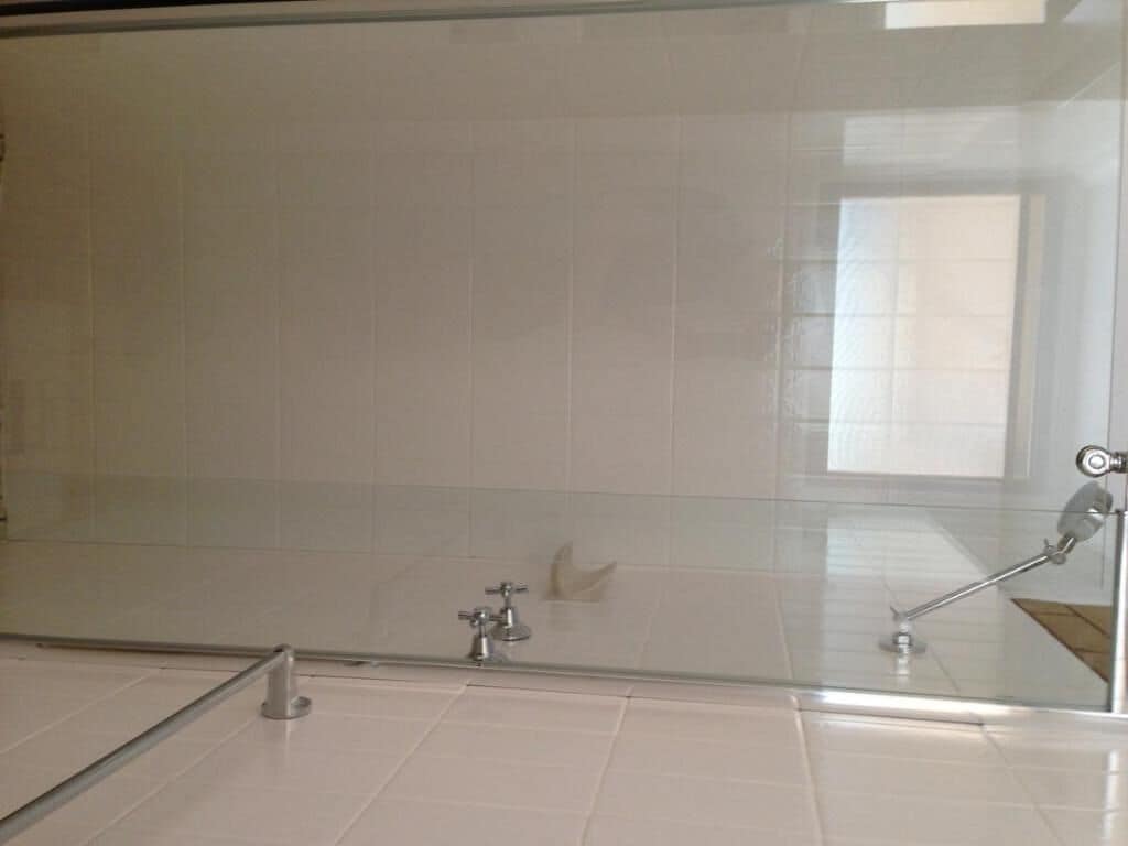 Une salle de bain avec des carreaux blancs, une douche en verre et un robinet apparent.