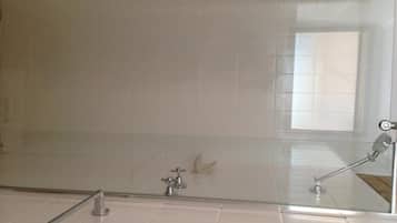 Un baño con azulejos blancos, cabina de ducha de cristal y grifo visible.