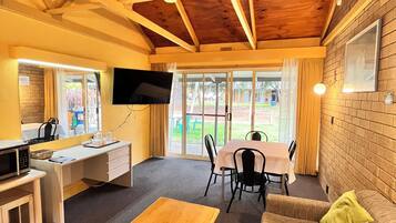 Ein Zimmer mit Holzboden, einem an der Wand befestigten Fernseher, einem Esstisch mit Stühlen, einer Couch und einem Couchtisch.