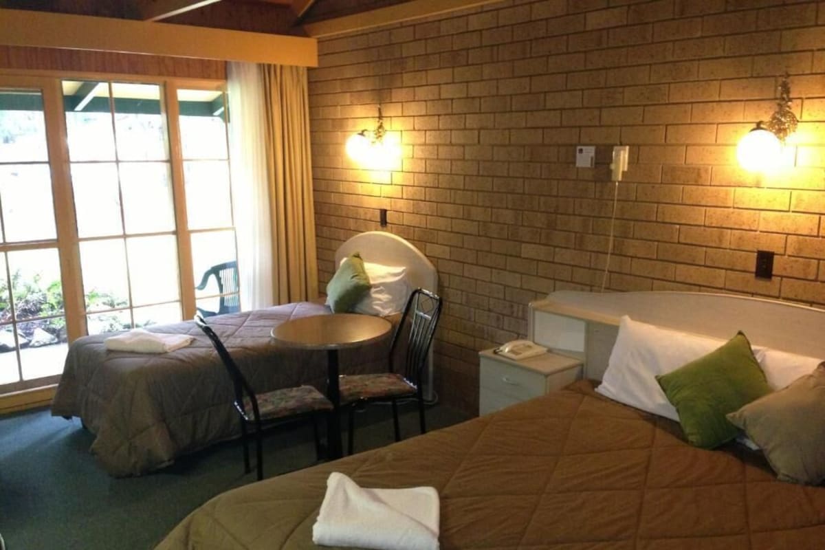 A hotel room with two beds, a small table, and a chair.